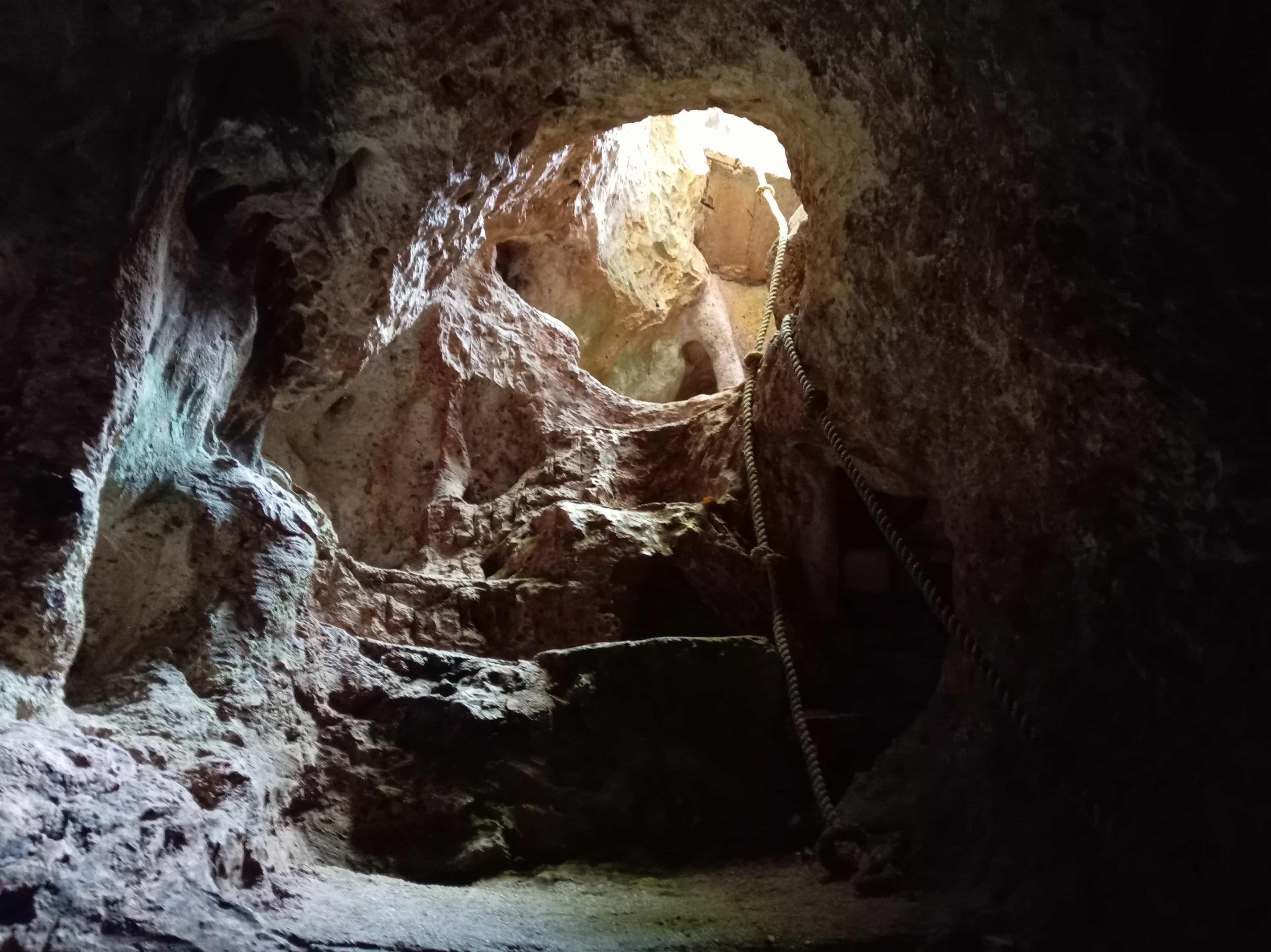 Túnel de roca con luz natural entrando y cuerda — cenote La Noria
